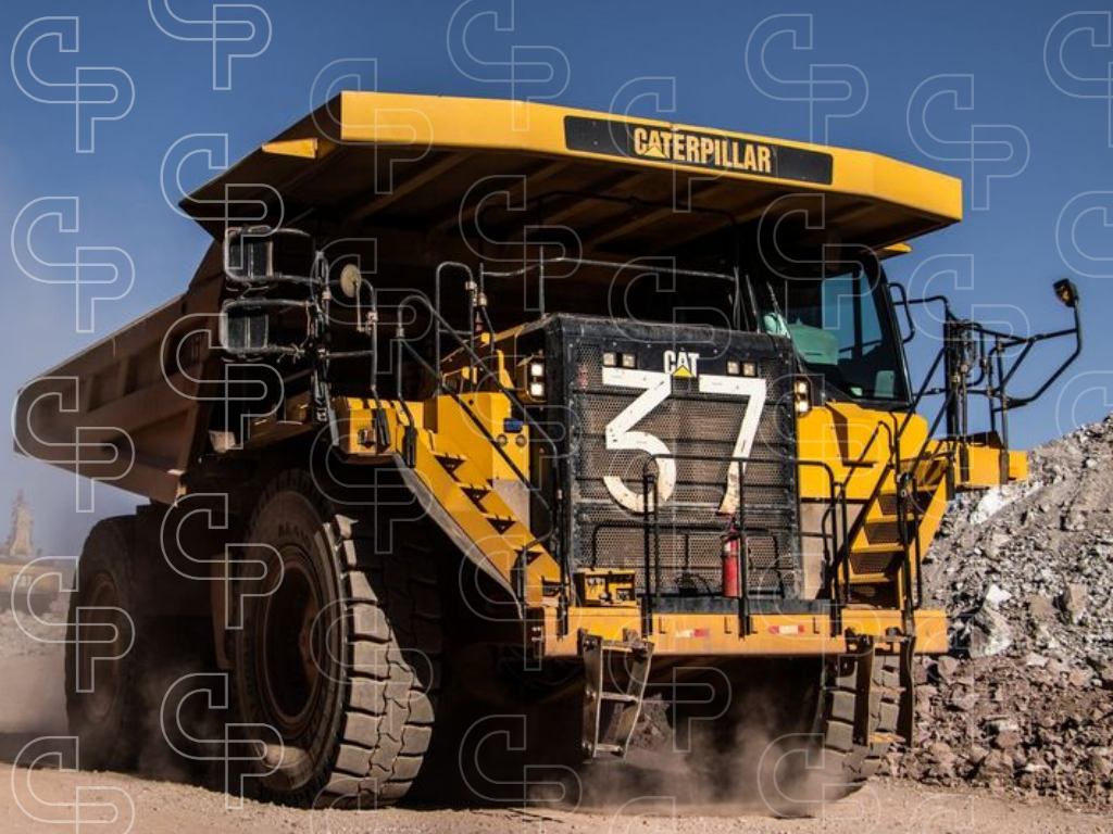Large Caterpillar haul truck driving through a rocky mine site with dust rising from the road.
