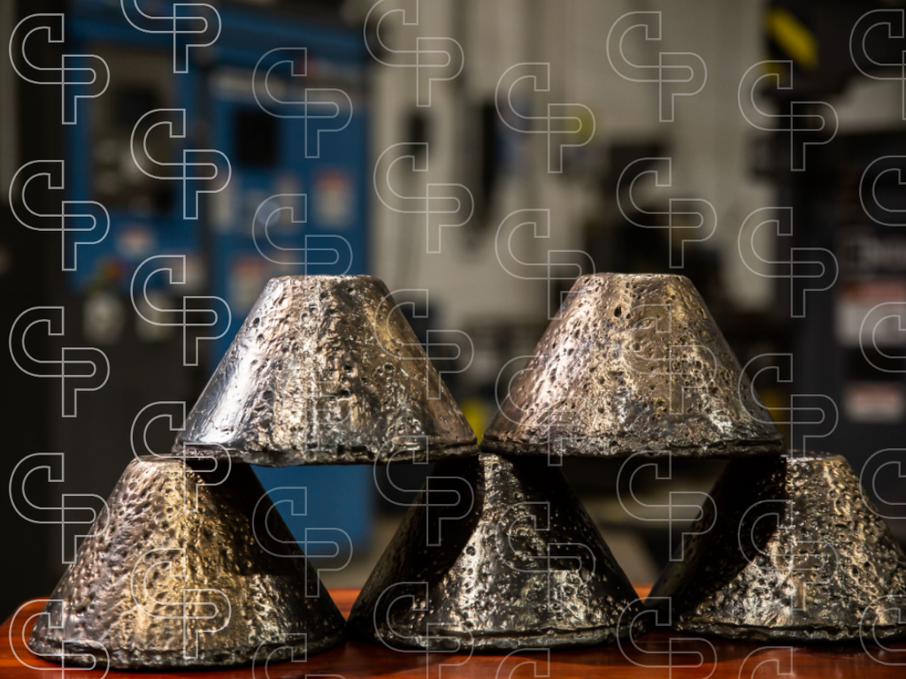 Stacked gold doré bars with rough metallic surfaces inside a refinery or metallurgical facility.