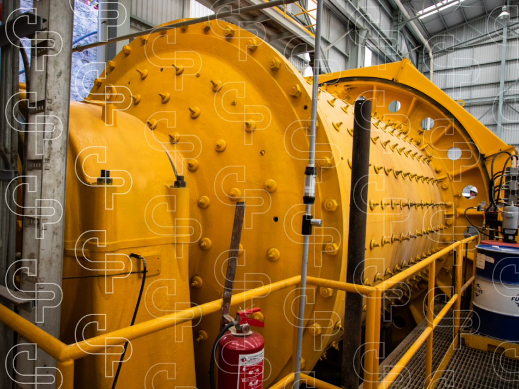 Large yellow industrial grinding mill with surrounding platforms and equipment inside a mineral processing facility.