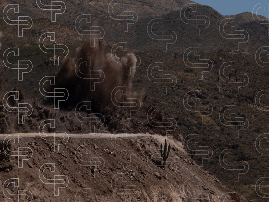 Controlled mine blast creating a large dust and debris cloud on a rocky hillside.