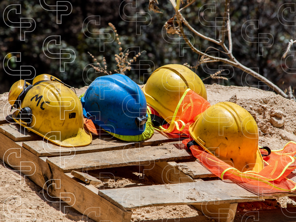 Yellow and blue mining hard hats and high visibility vests laid on timber at a dusty work site.