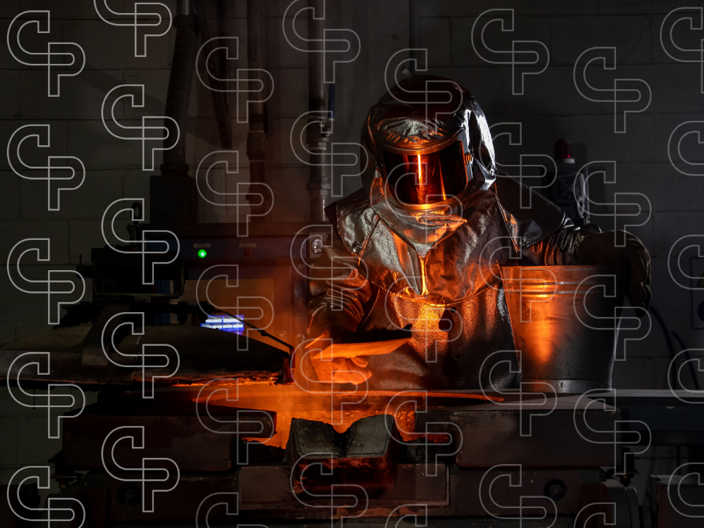 Person wearing a heat protective suit pouring glowing molten metal inside an industrial foundry.