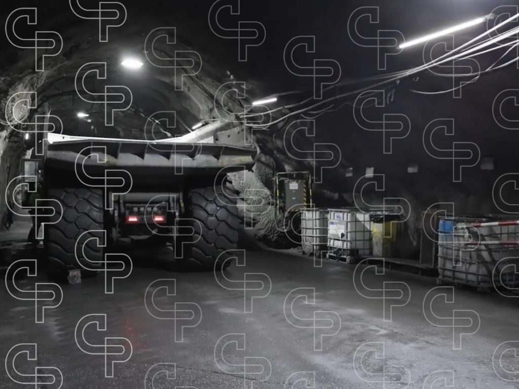 Haul truck parked inside an underground mine tunnel with rock walls, cables and industrial lighting.